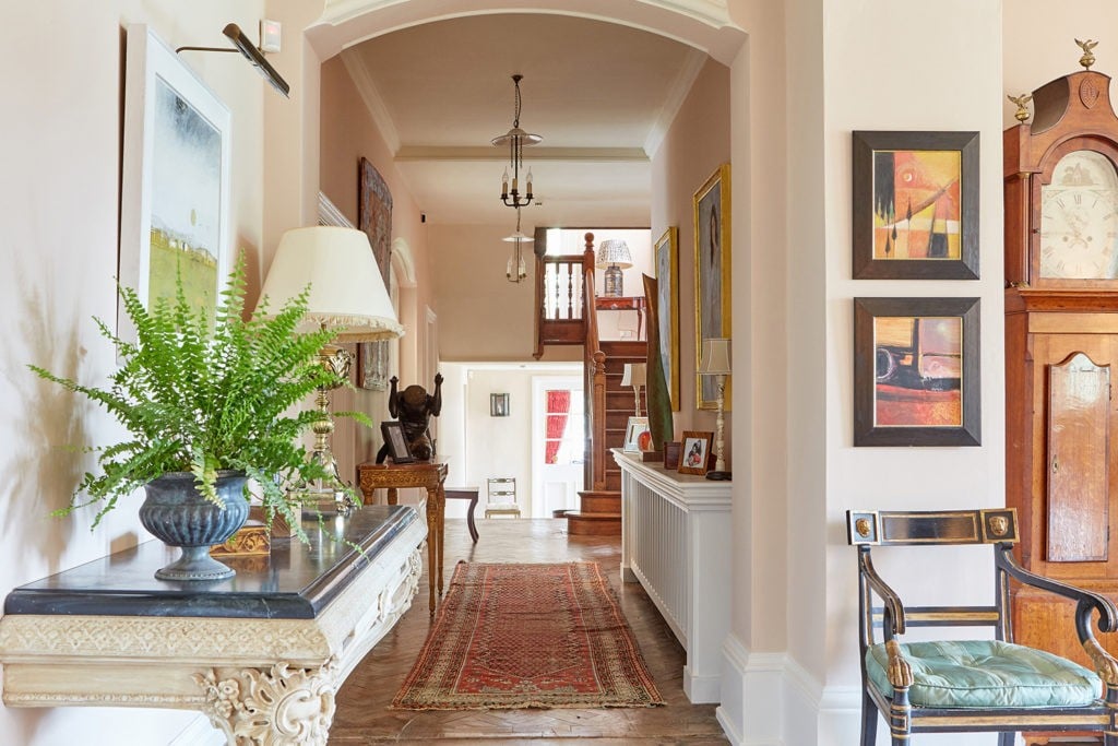 Hallway in light pink with grandfather clock, archway and green plants of side table