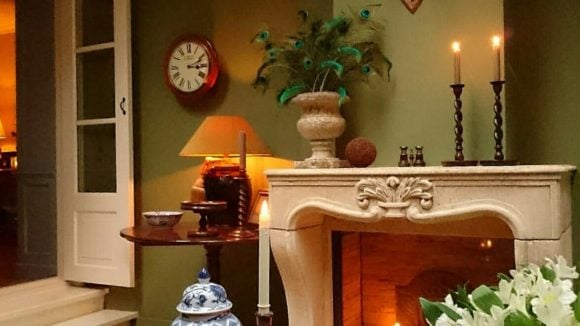 Sitting room in deep green tones with candles lit on a mantel piece.