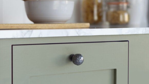 Kitchen cabinet painted in green with pestle and mortar on top of it.